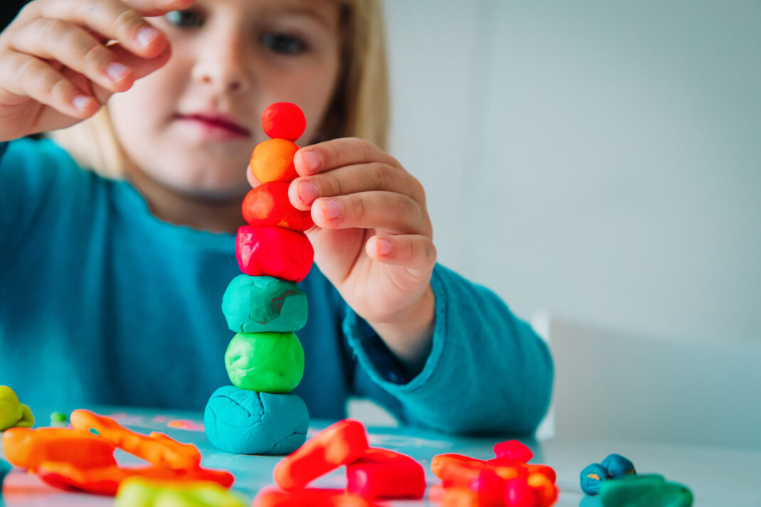 Child stacking colorful clay balls on a table.