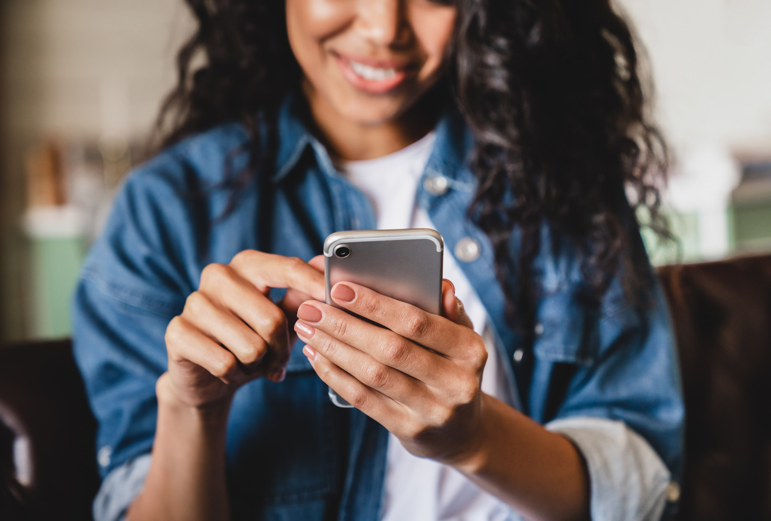 A person in a denim jacket smiles while using a smartphone.